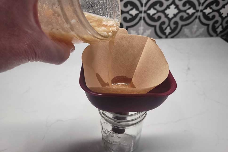 Straining bacon fat-washed bourbon through a coffee filter to remove the fat solids.