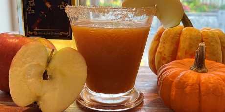 Cozy fall pumpkin cocktail on counter with a bottle of whisky, gourds, and apples.