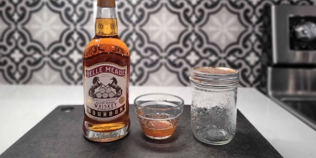A bottle of bourbon and a small bowl of bacon fat on a counter.